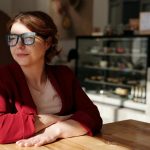 Woman in a wheelchair enjoying a sunny day at a café, wearing eyeglasses and a red jacket.